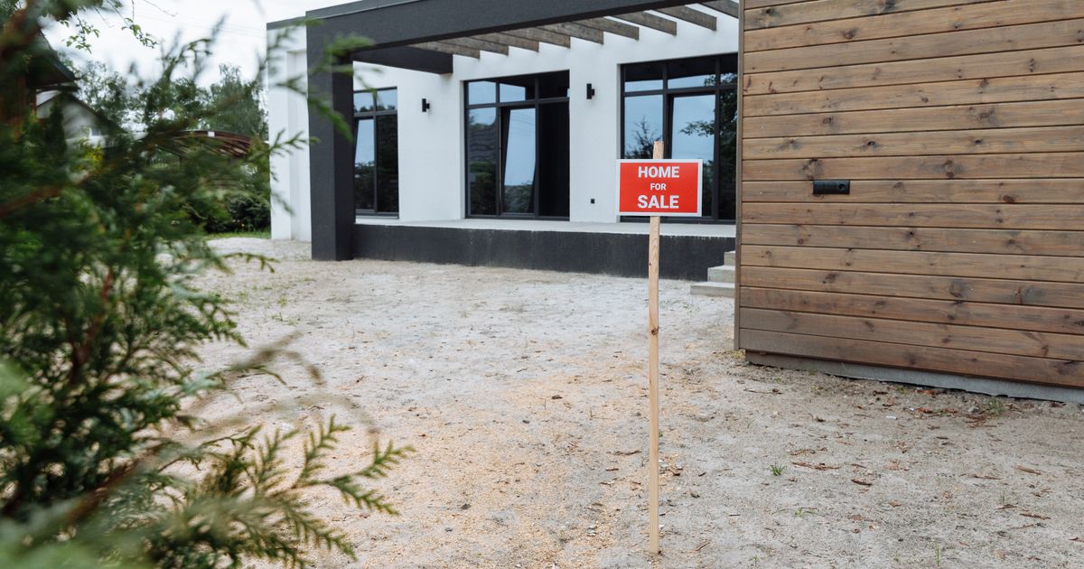 A modern home with a red Home For Sale sign on the front lawn